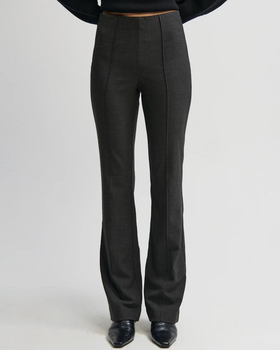 A person wearing dark charcoal gray high-waisted flared trousers, paired with a black top and black shoes, shown from the waist down against a light gray studio background.
