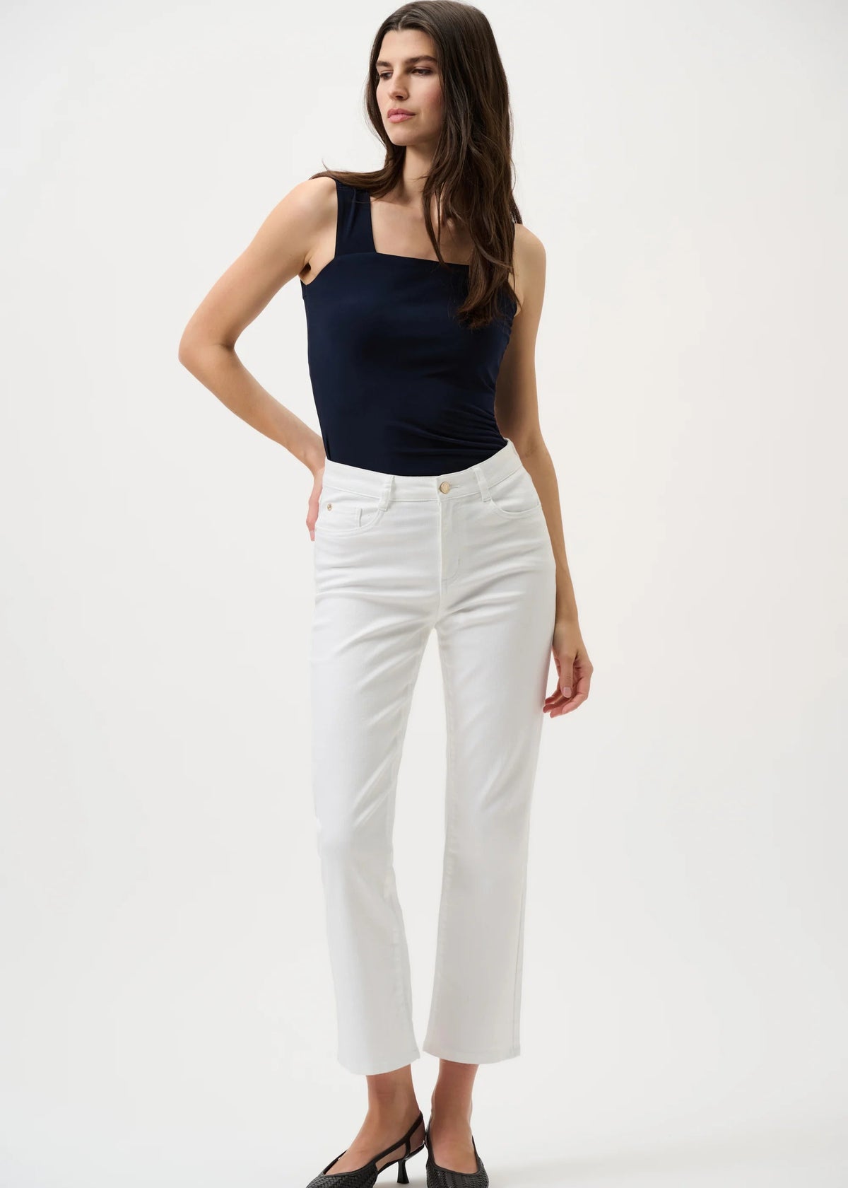 Woman wearing a navy tank top and white pants on a white background