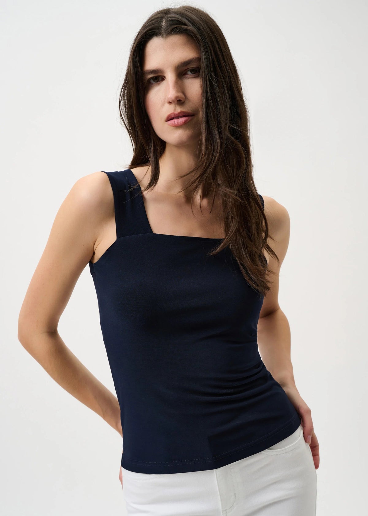 Woman wearing a navy blue tank top and white pants on a white background