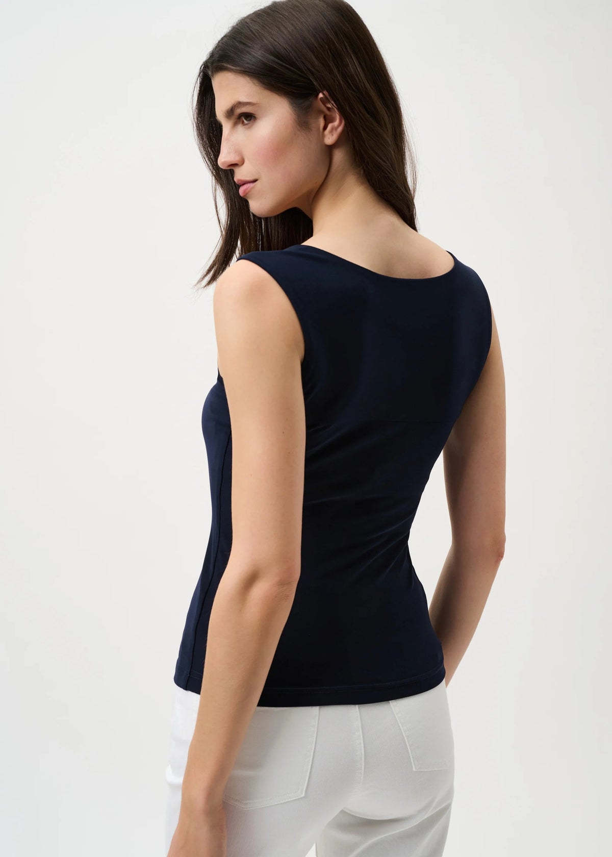 Woman wearing a navy sleeveless top and white pants on a light gray background