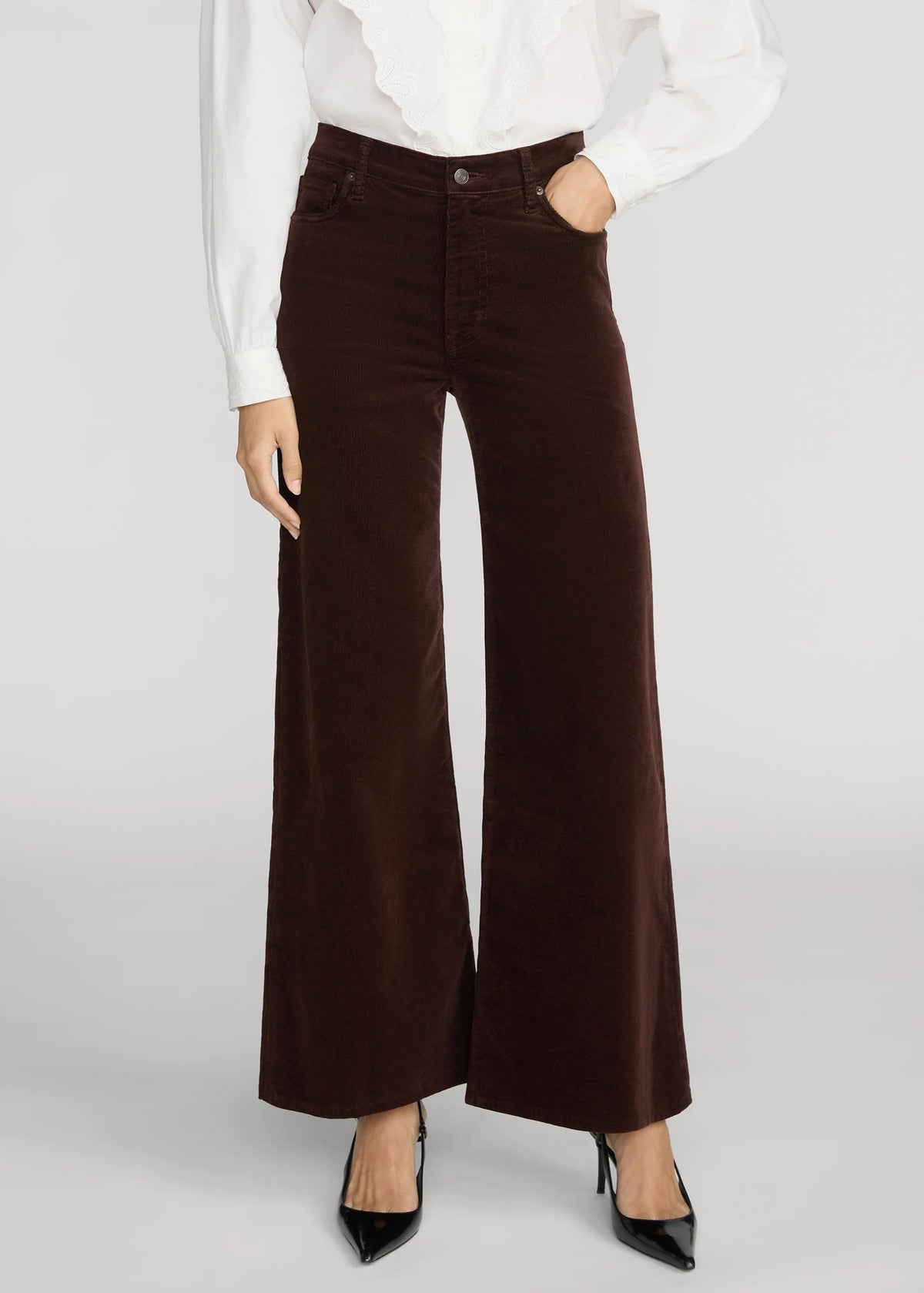 A model wearing high-waisted, wide-leg brown corduroy pants, styled with a white blouse and black heels, against a light gray studio background.