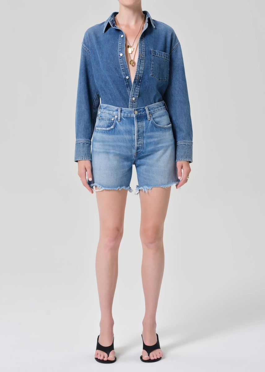 Person wearing a denim shirt and shorts on a white background