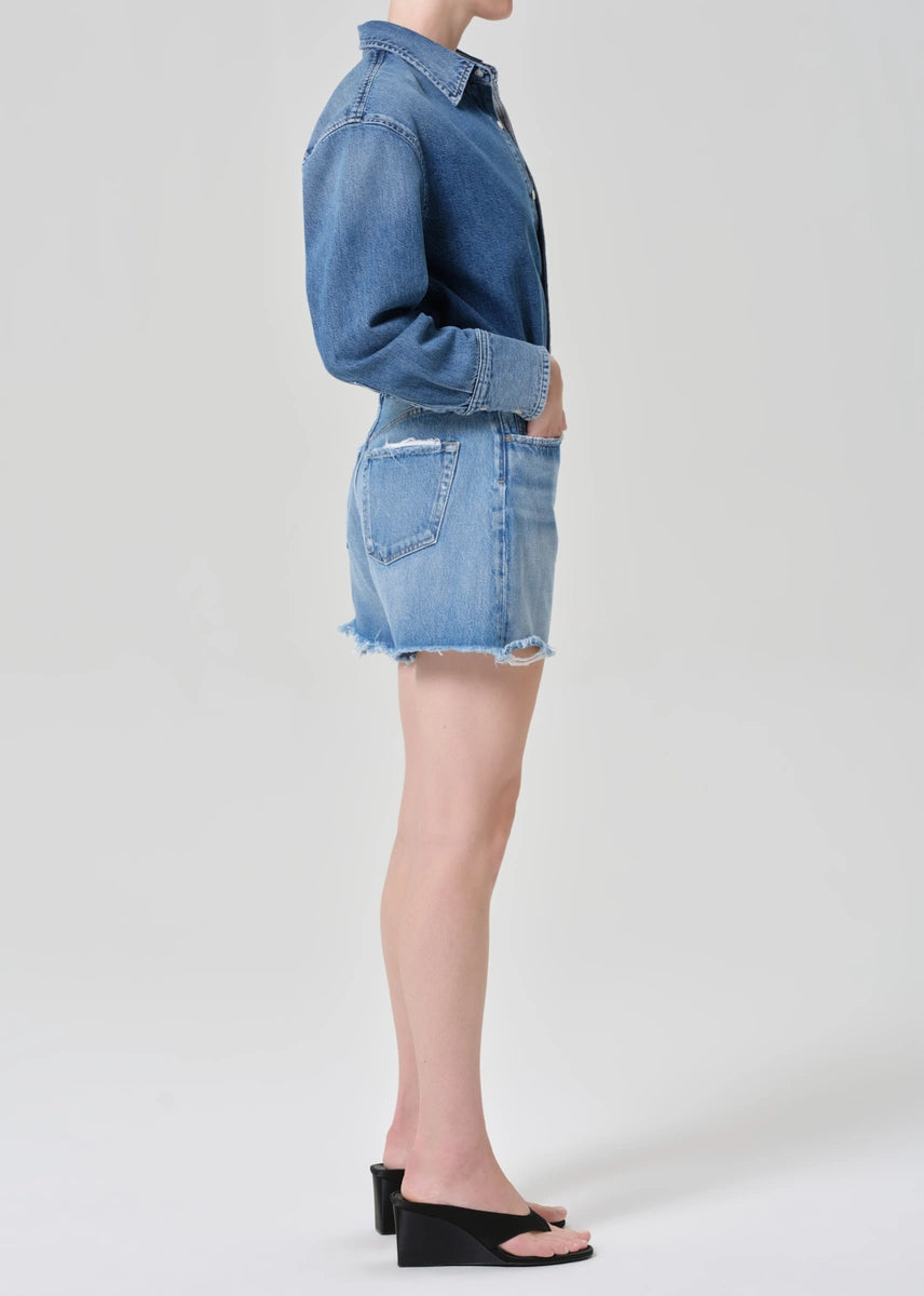 Person wearing a denim jacket and shorts on a white background