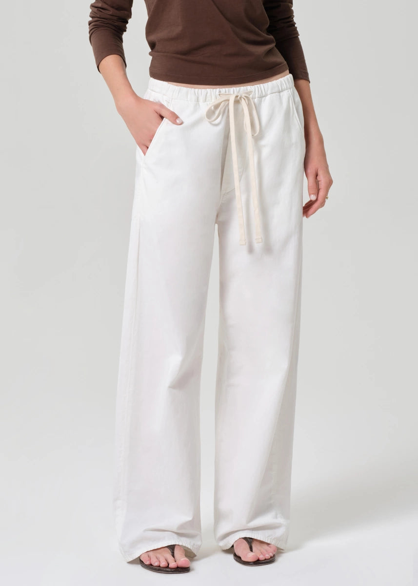 Person wearing white wide-leg pants and a brown top on a plain background