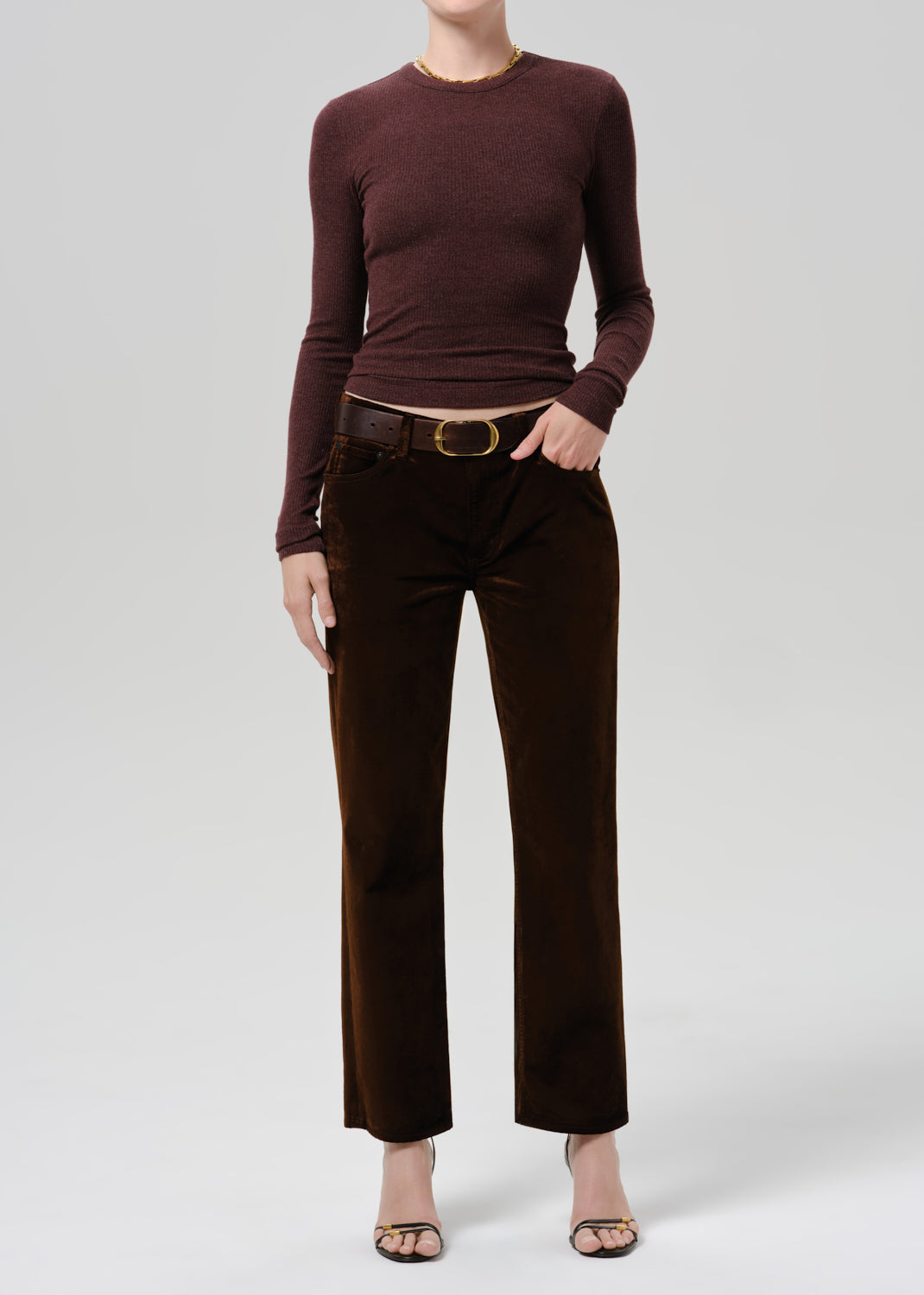 A model wearing a dark brown long-sleeve knit top and matching dark brown wide-leg trousers with a brown belt, shown against a light gray studio background.
