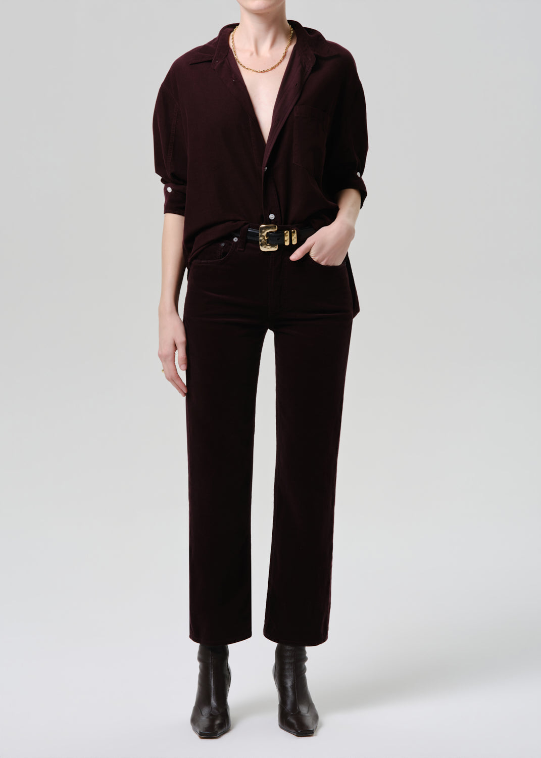 Person wearing a dark brown outfit with a belt and boots on a white background