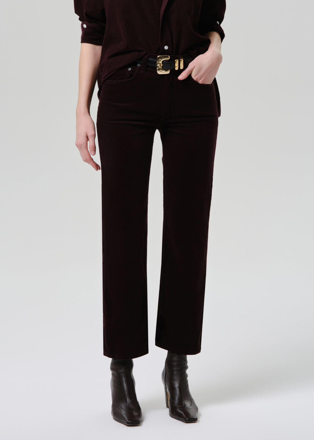 Person wearing black pants with a gold belt on a white background