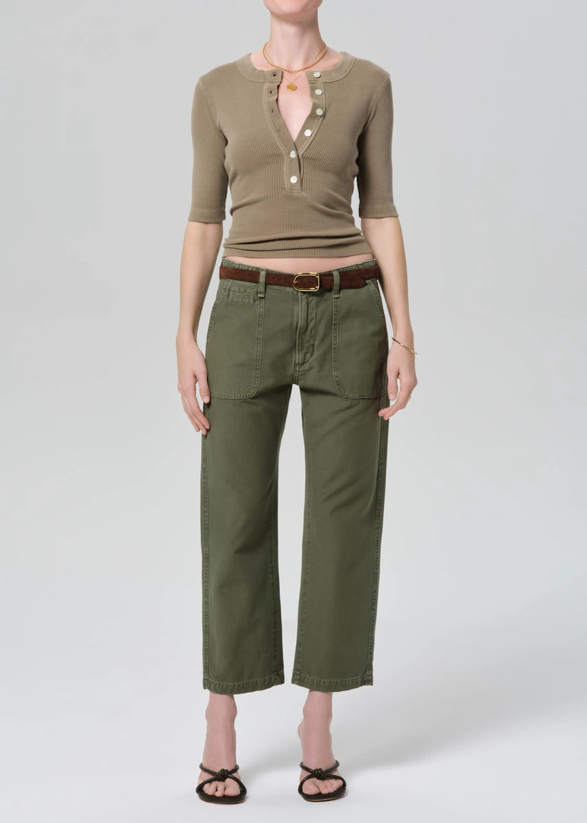 Person wearing a beige top and green pants on a white background