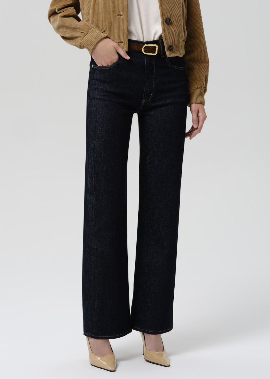 Person wearing black wide-leg jeans with a brown jacket and beige shoes on a white background