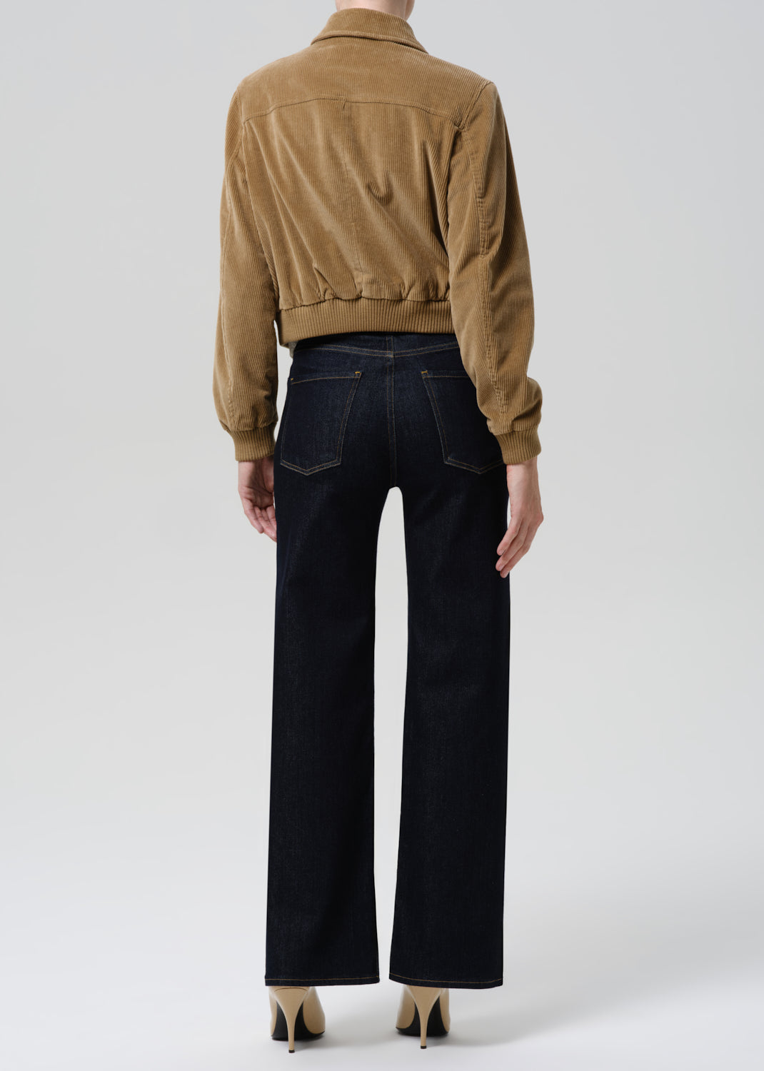Person wearing a brown jacket and black pants on a white background