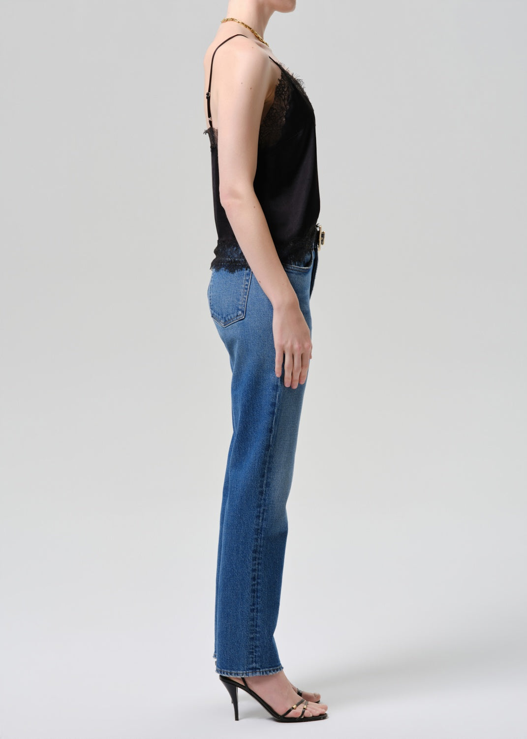 Person wearing a black sleeveless top and blue jeans on a light gray background