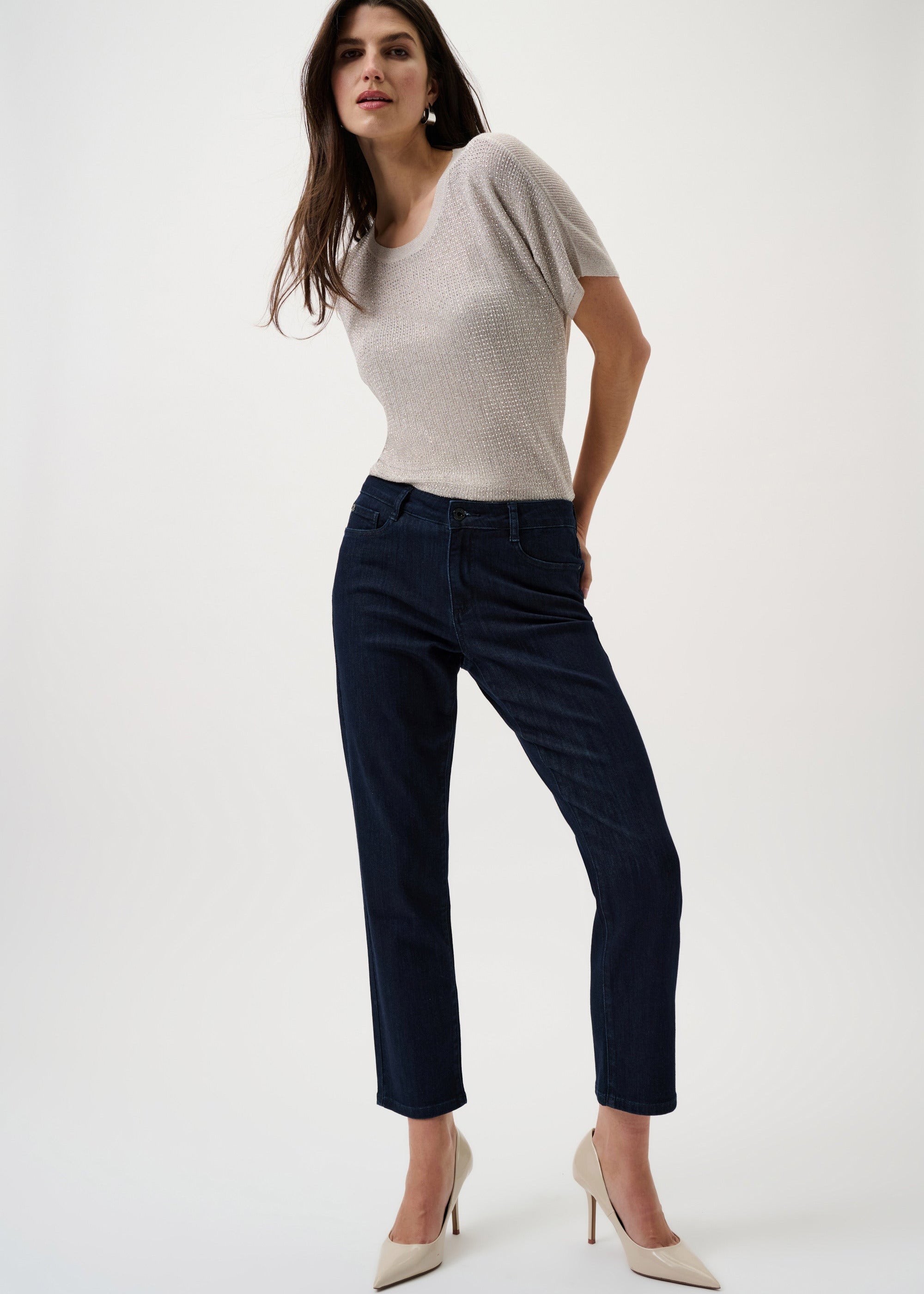 Woman wearing a beige top and dark blue jeans on a white background