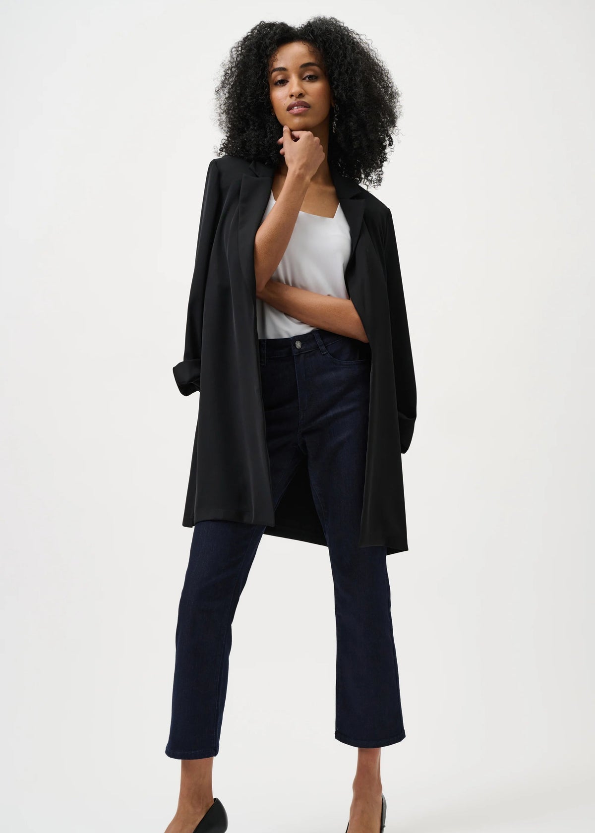 Woman wearing a black coat, white top, and dark pants on a white background