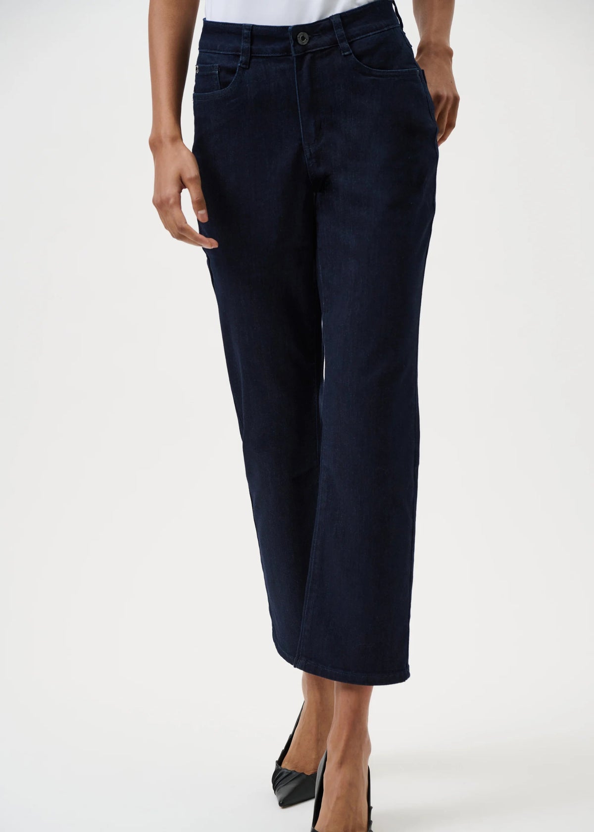 A model wearing dark navy blue cropped jeans with a straight-leg fit, paired with black pointed-toe heels, shown from the waist down on a white studio background.