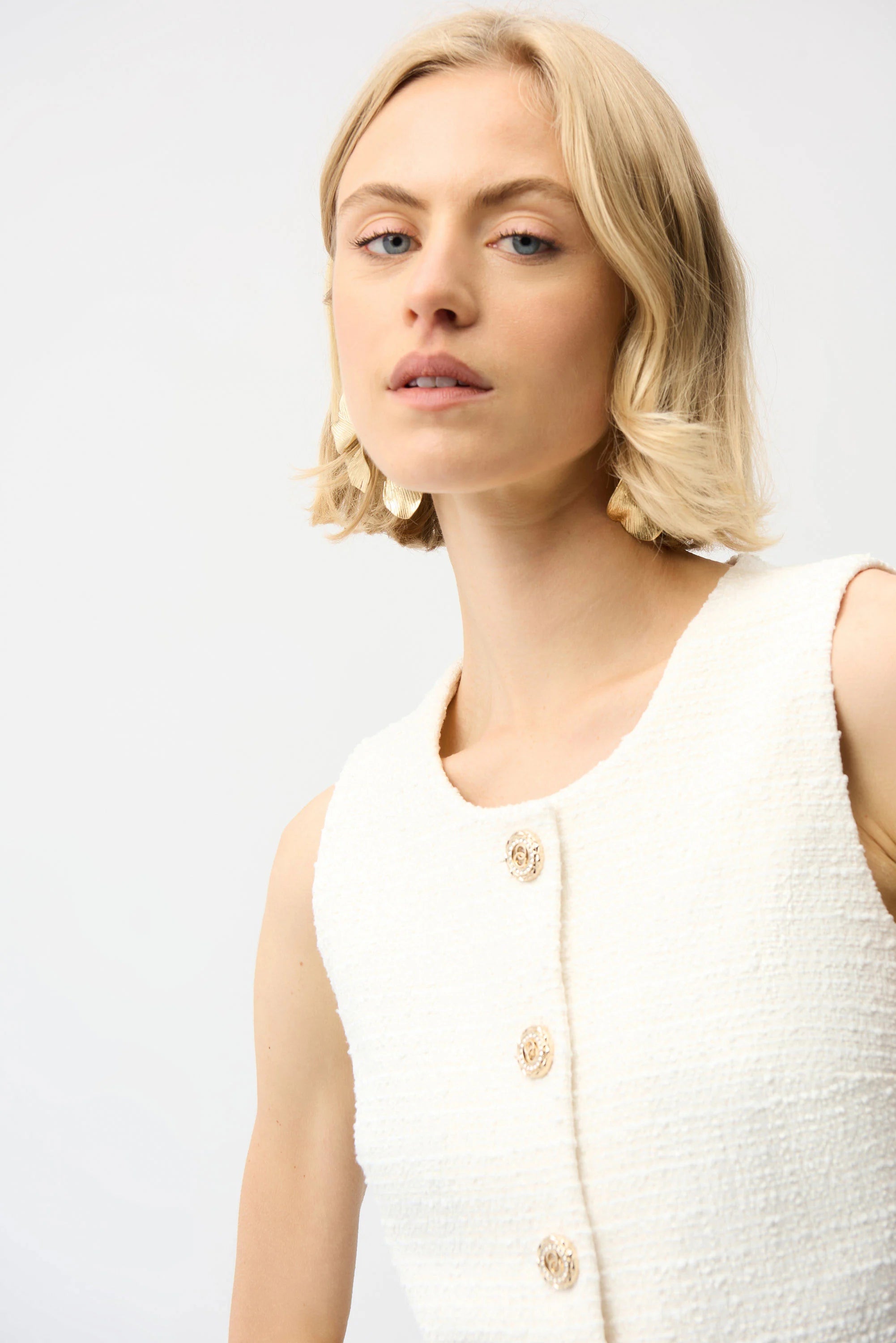 Woman wearing a white sleeveless textured top against a plain background
