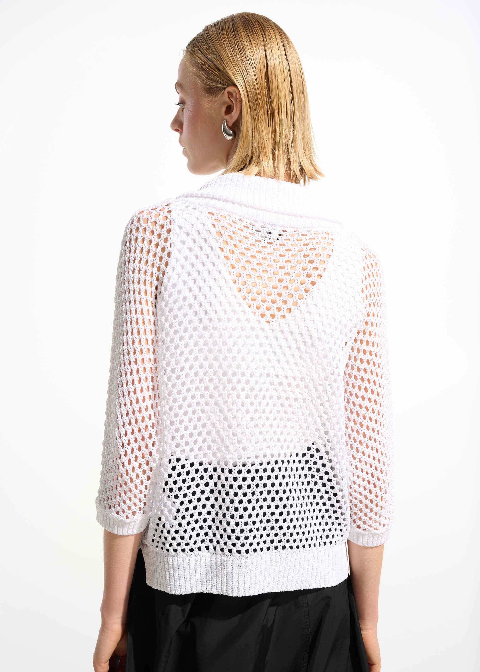 Woman wearing a white mesh top with black polka dot pattern on a plain background