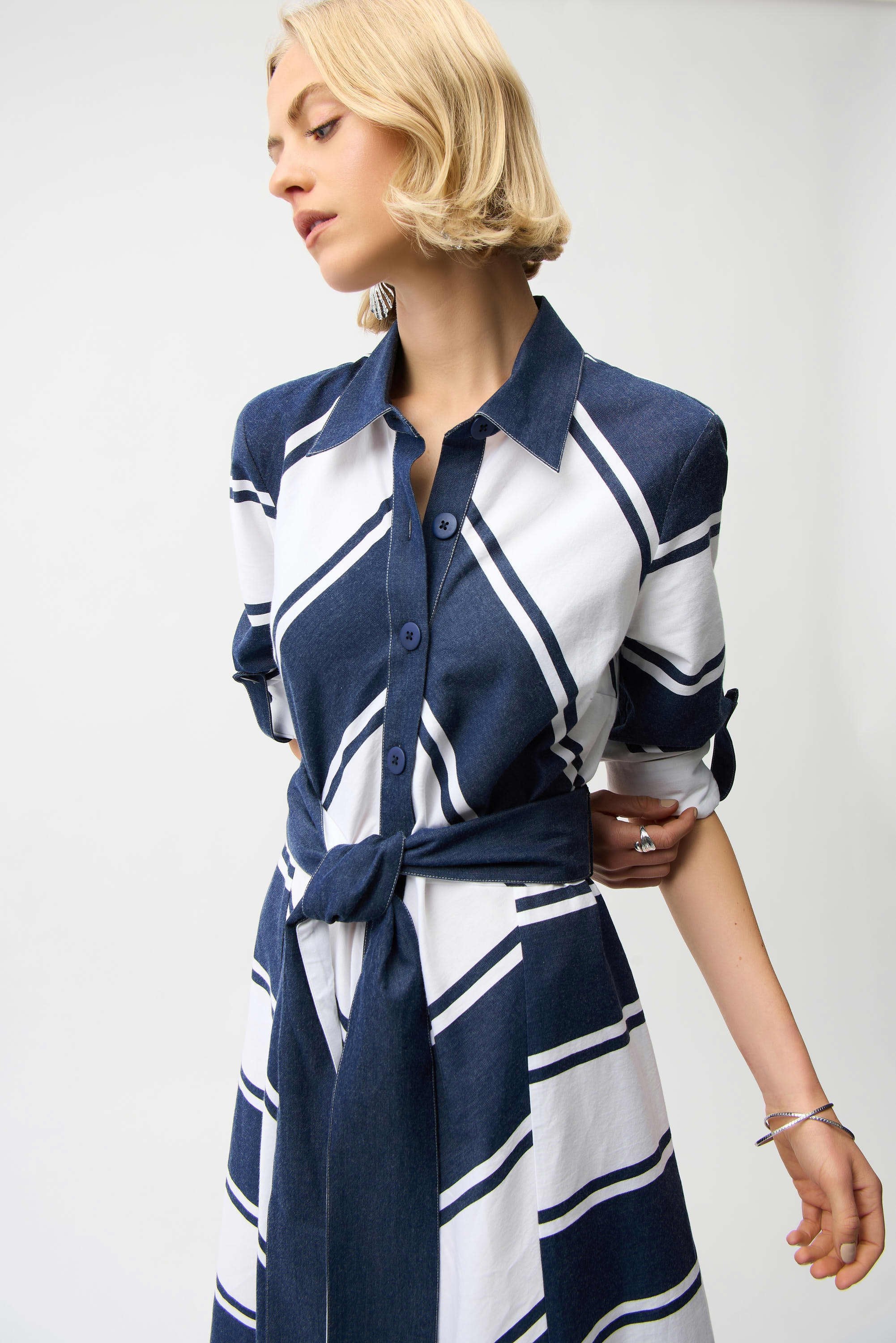 Woman wearing a blue and white striped dress with a tie waist on a plain background