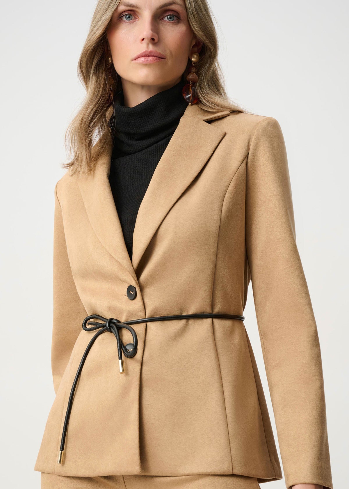 Woman wearing a beige suit with a black turtleneck on a white background