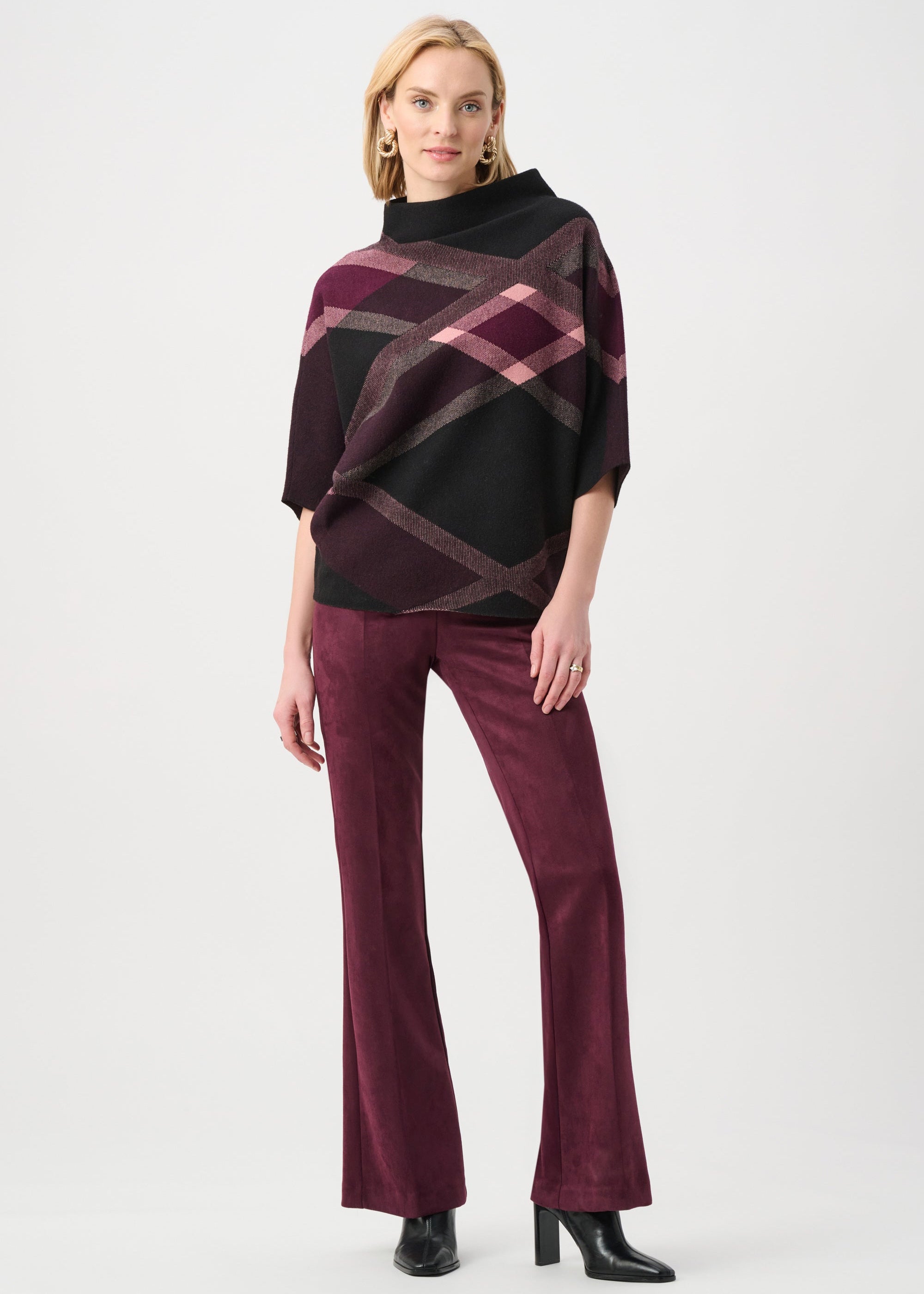 Woman wearing a patterned poncho and burgundy pants on a white background