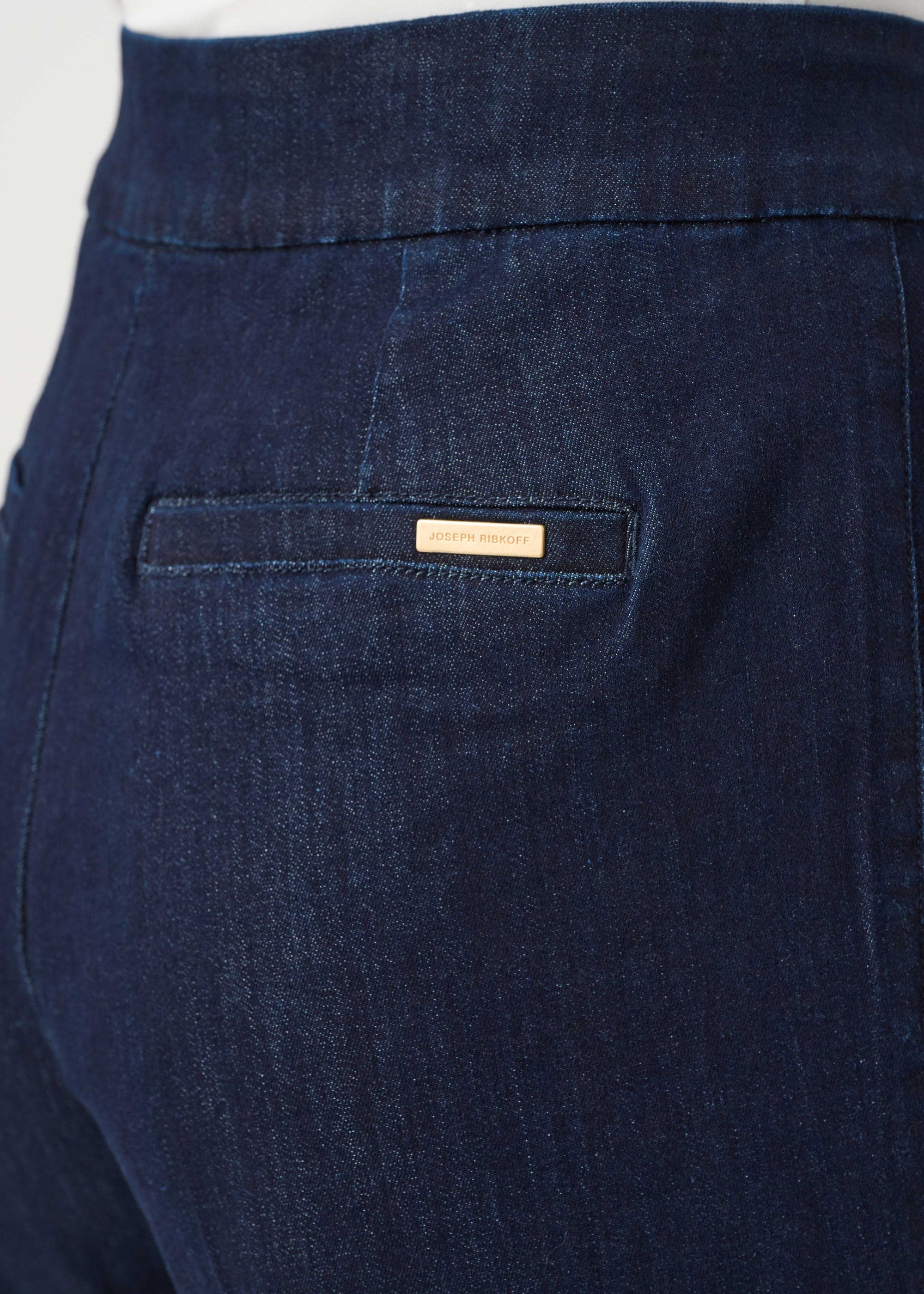 Close-up of dark blue pants with a brand label on the pocket against a white background
