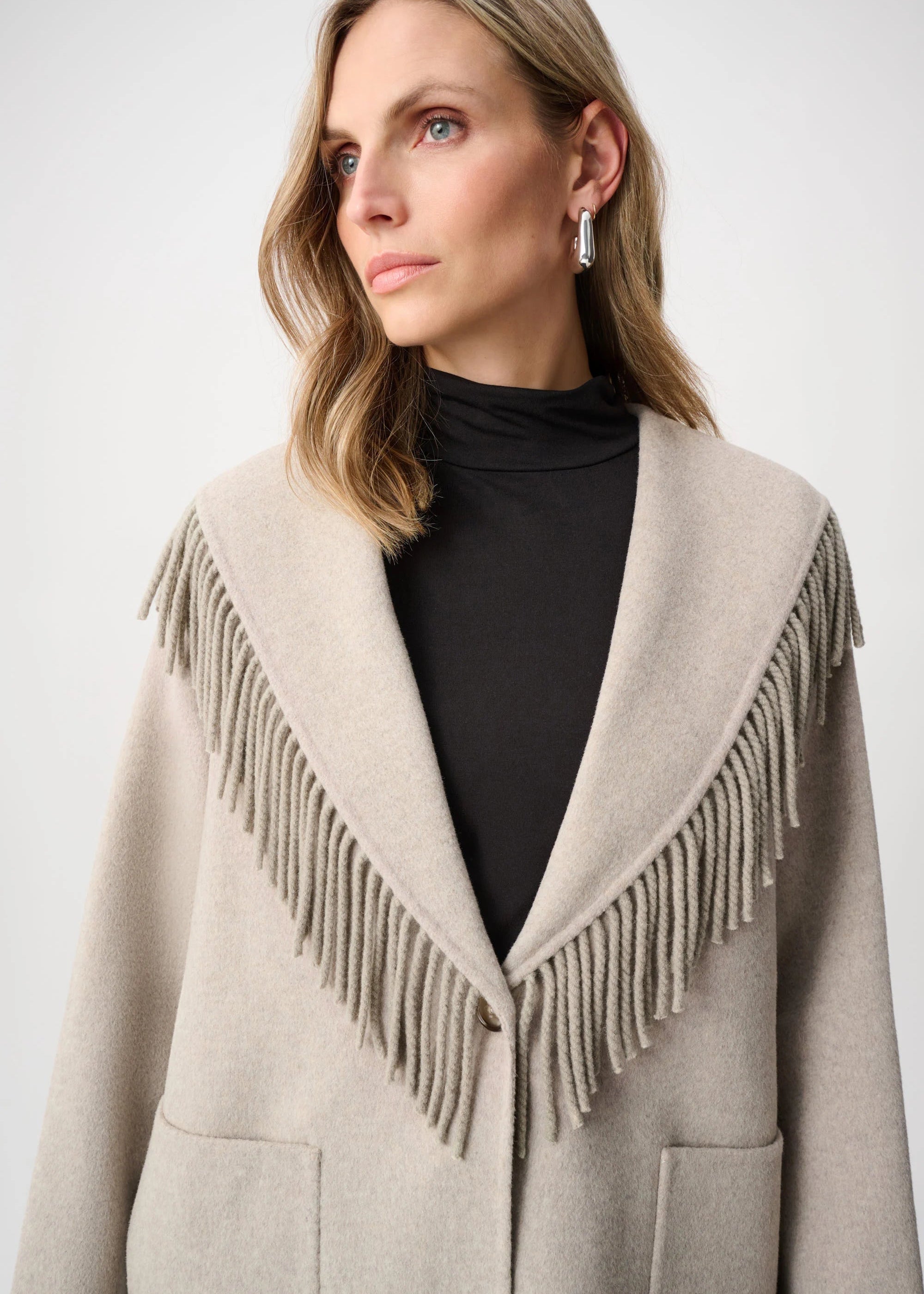 Woman wearing a beige coat with fringe details on a white background