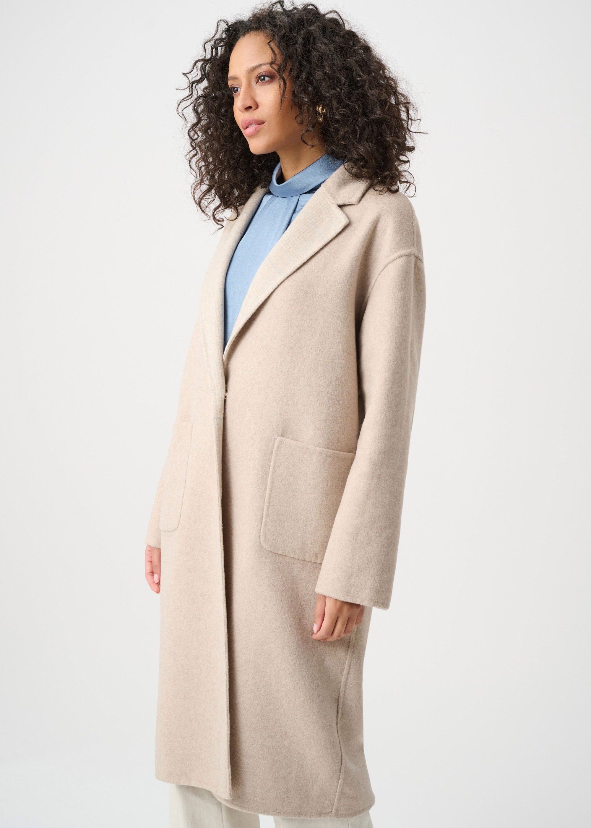Woman wearing a beige coat over a blue sweater on a white background