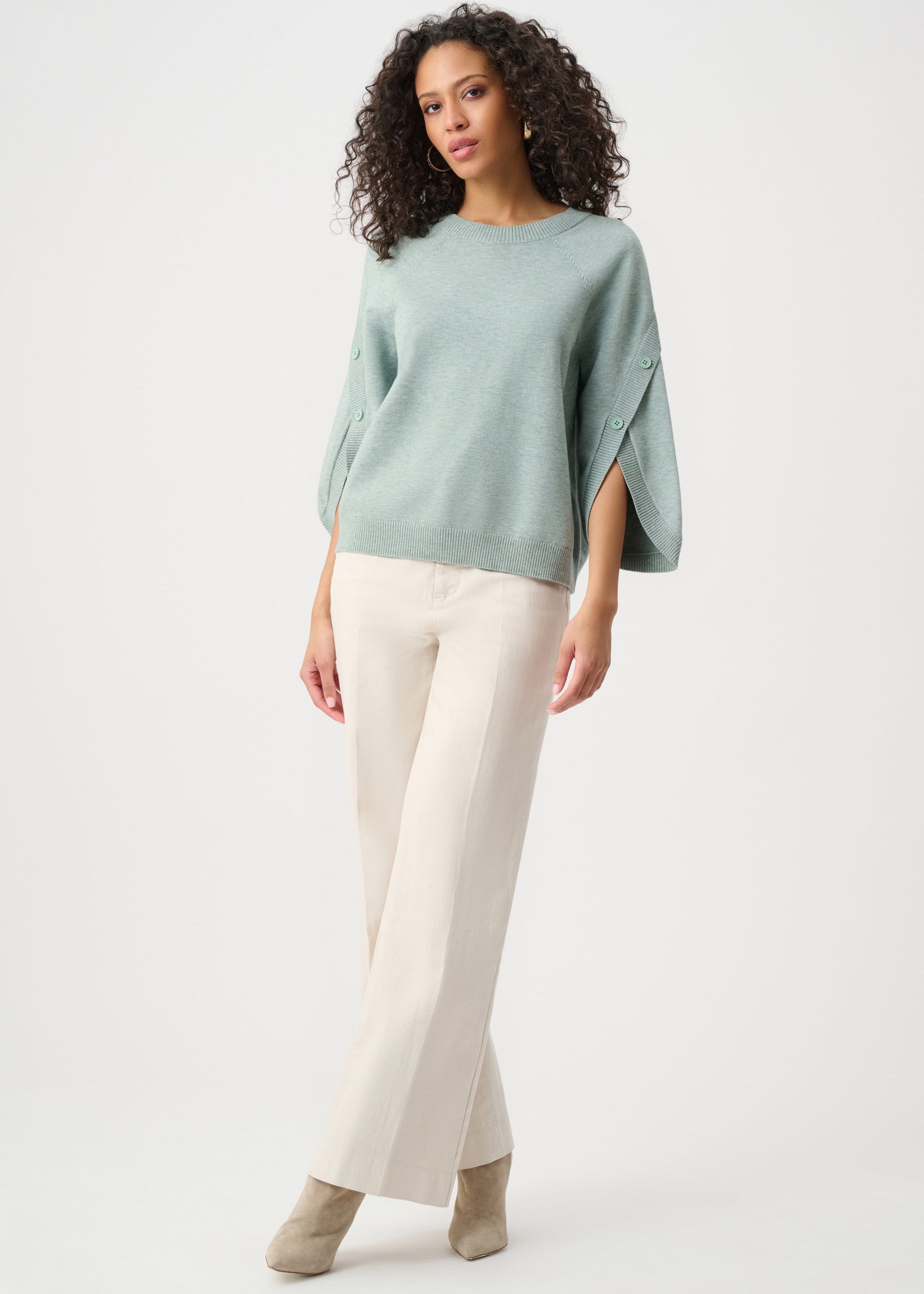 Woman wearing a light green sweater and white pants on a white background