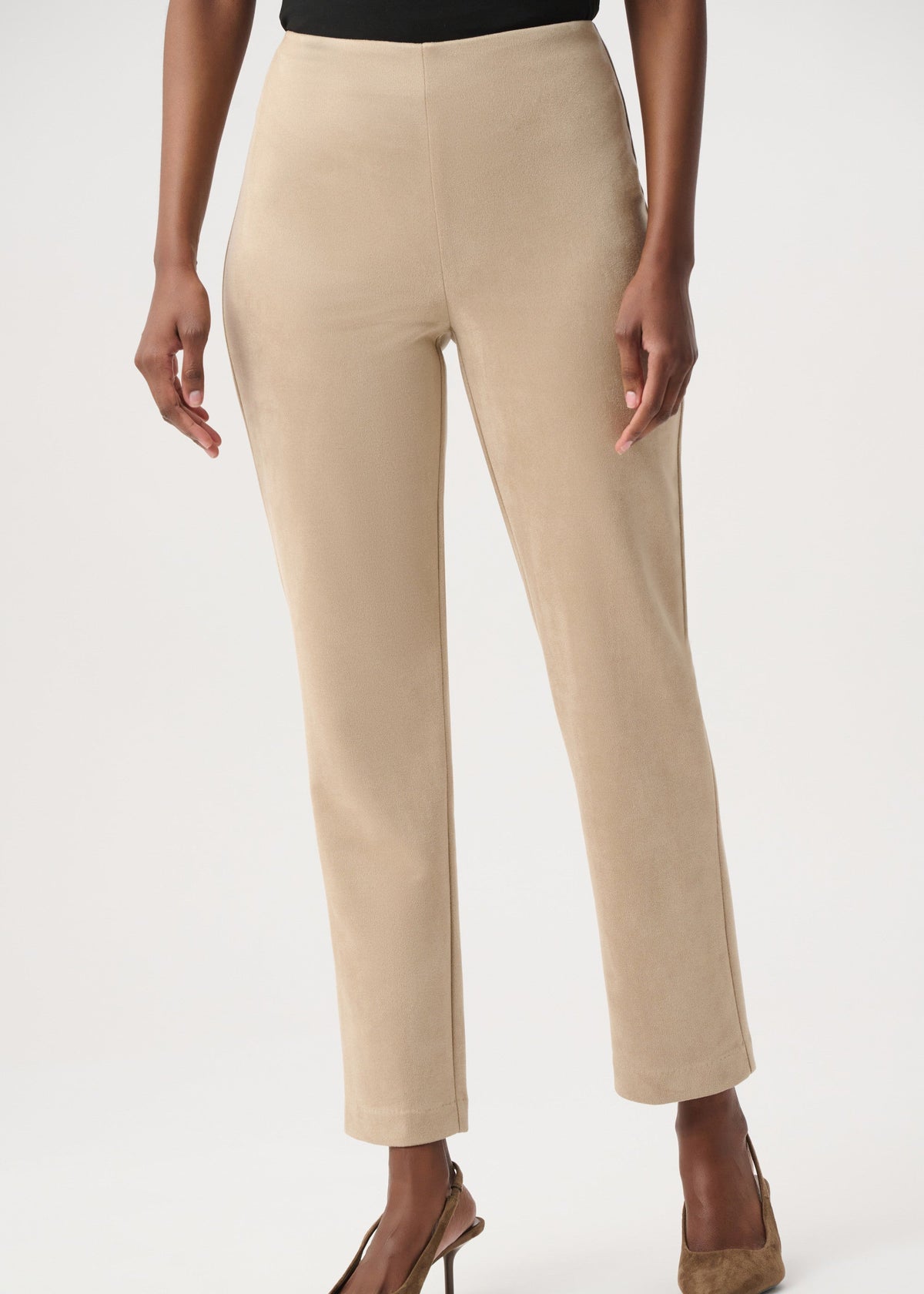 A model wearing a pair of straight-leg, ankle-length cropped pants in a light beige color, paired with brown pointed-toe stiletto heels against a plain light gray studio background.