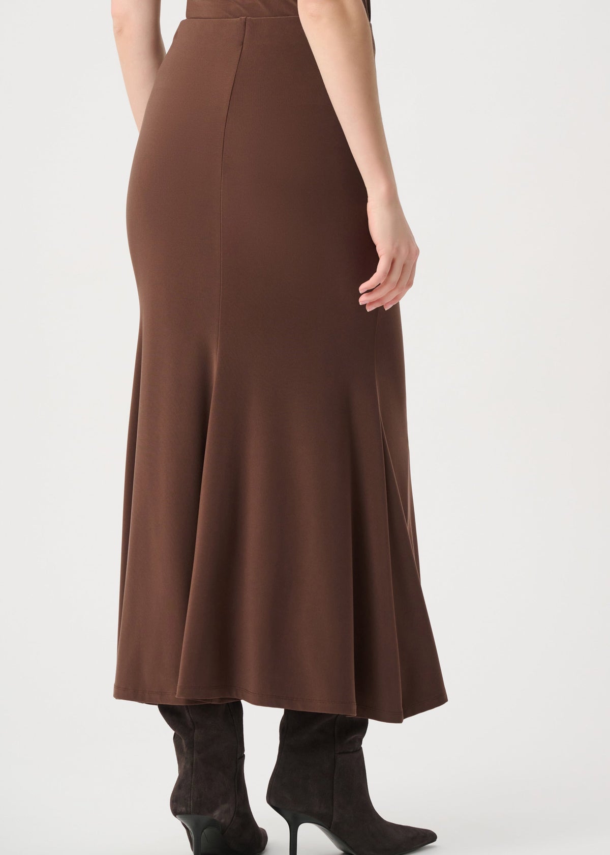 A woman wearing a brown high-waisted flared midi skirt and dark brown heeled ankle boots, shown from the back against a light gray studio background.