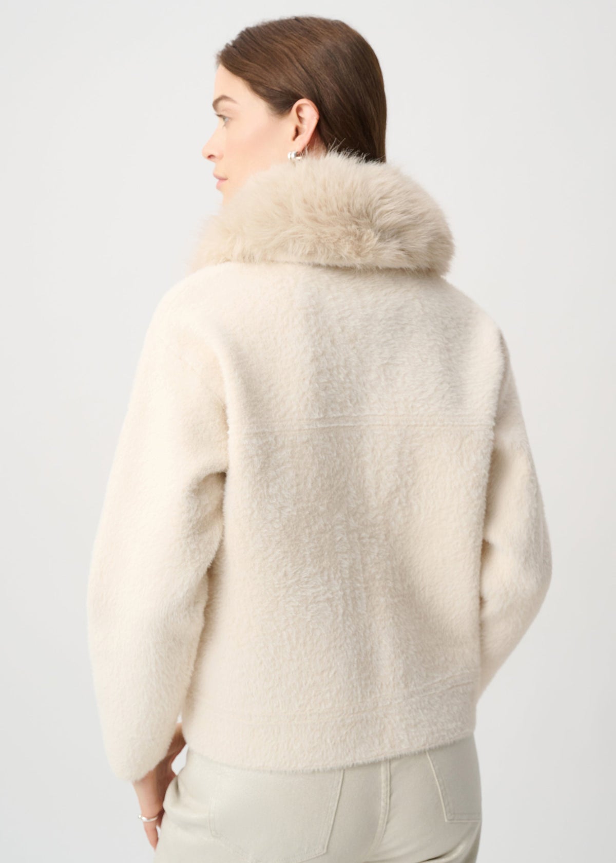 Person wearing a cream-colored jacket with fur collar on a light gray background