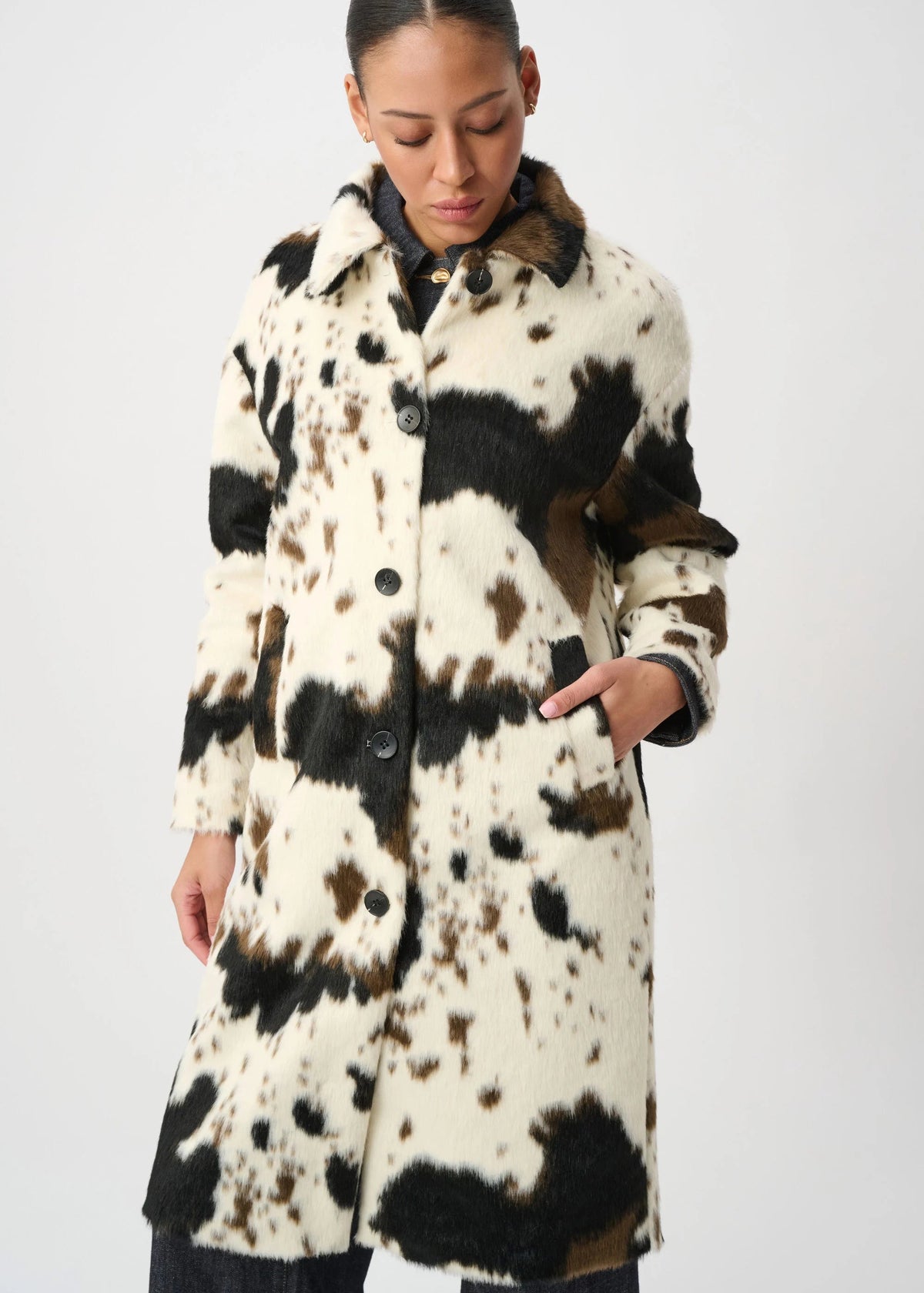 Woman wearing a long, patterned coat with black, white, and brown colors on a plain background.