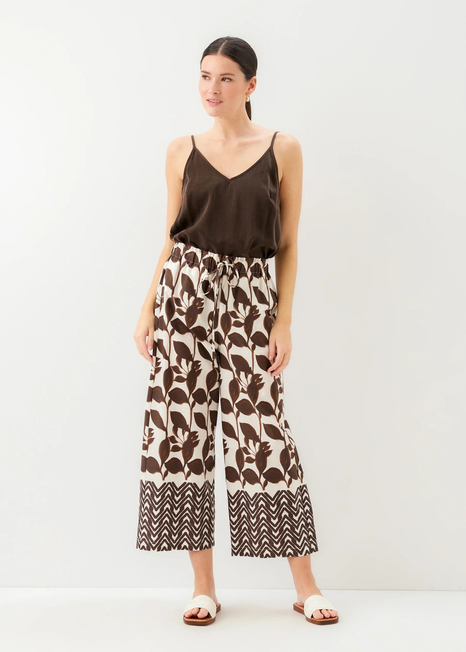 Woman wearing a brown top and patterned pants on a white background