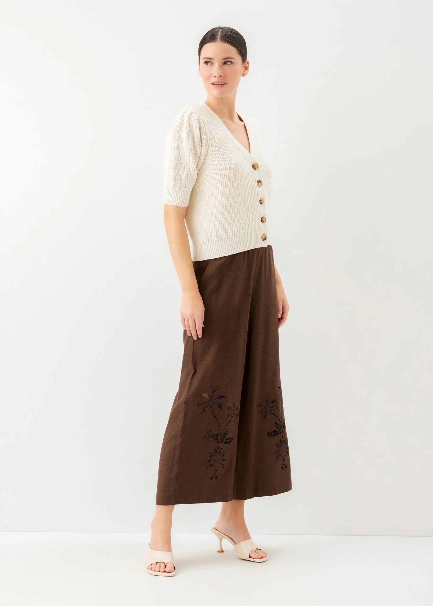 Woman wearing a cream top with buttons and a brown skirt with floral embroidery on a white background