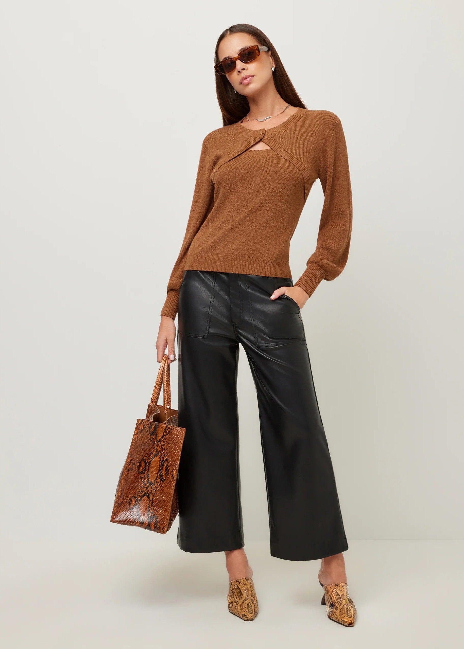 A woman modeling a brown knit long-sleeve top with a chest cutout, paired with black wide-leg pants, leopard-print pointed shoes, sunglasses, and a brown snakeskin tote bag, against a light gray studio background.