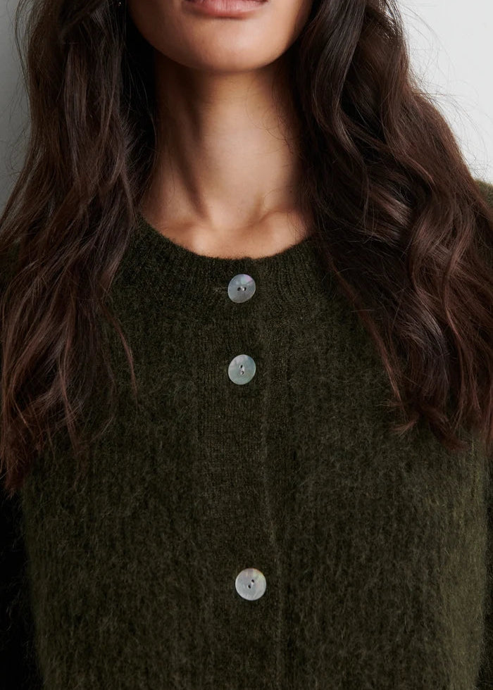Close-up of a person wearing a dark green cardigan with button details.