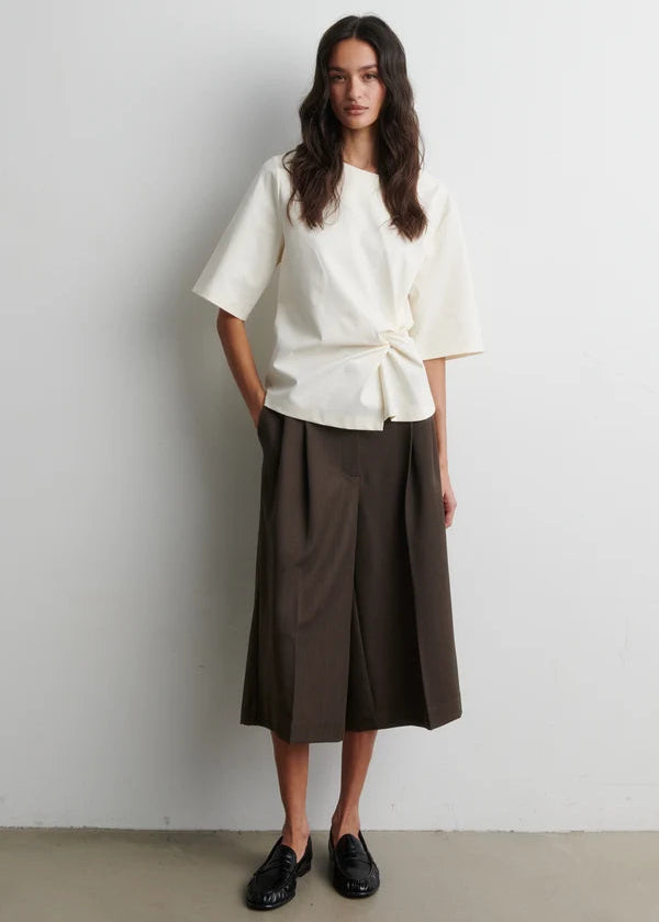Woman wearing a white top and brown pants against a plain background
