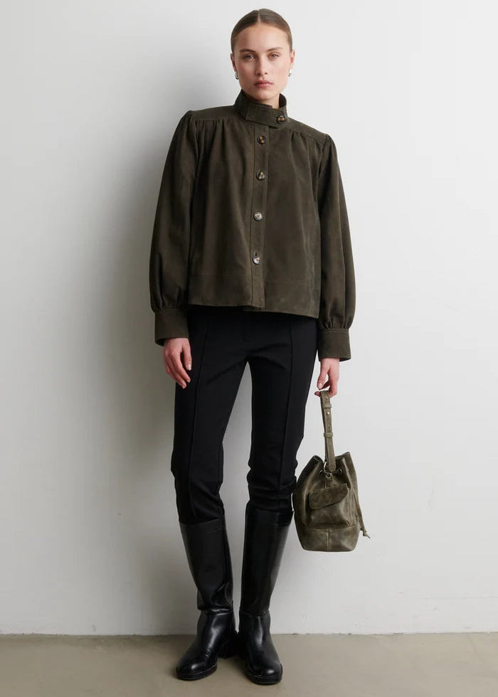 Person wearing a dark green jacket, black pants, and boots, holding a matching bag against a white background.