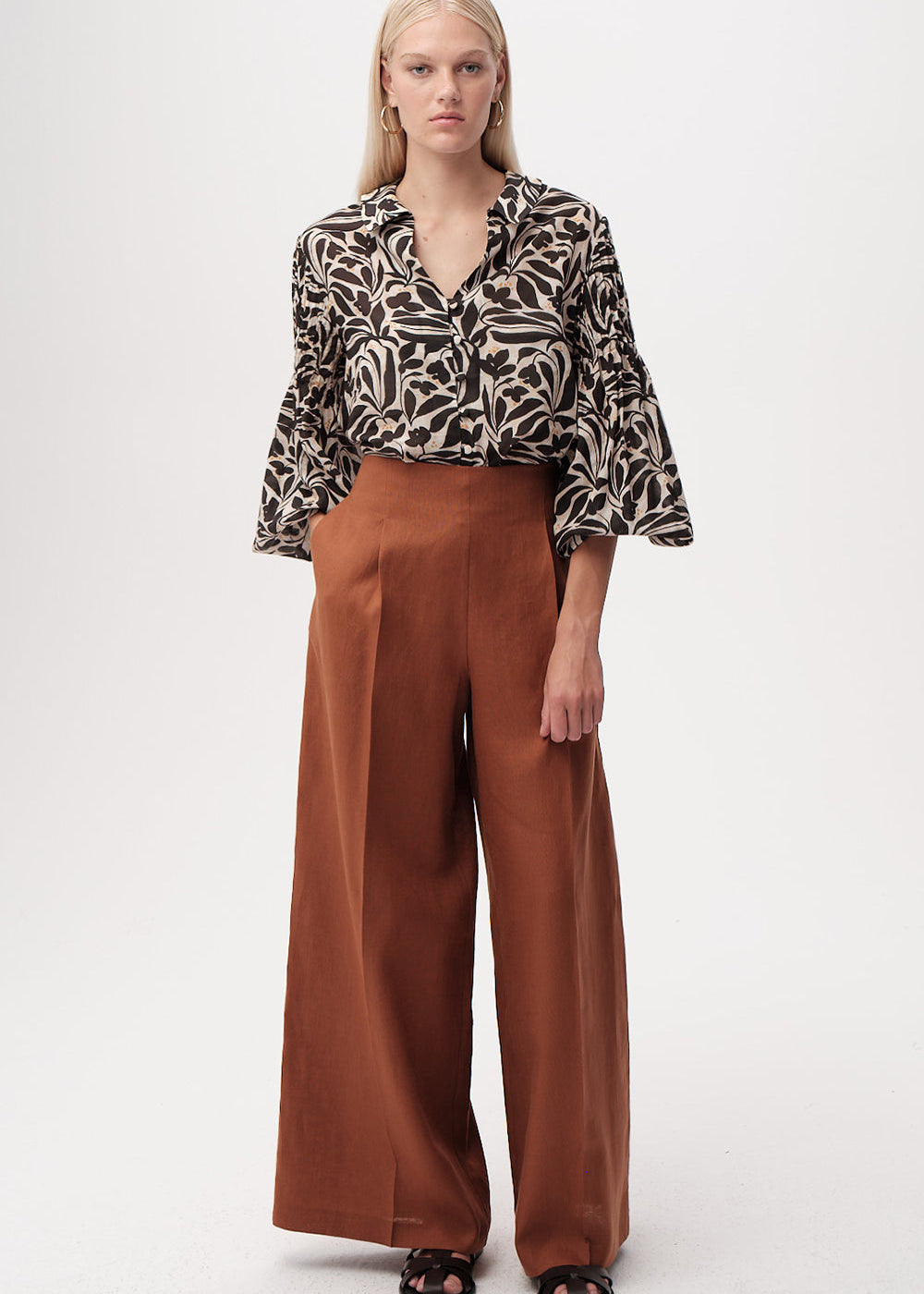 Woman wearing a patterned blouse and brown wide-leg pants on a white background