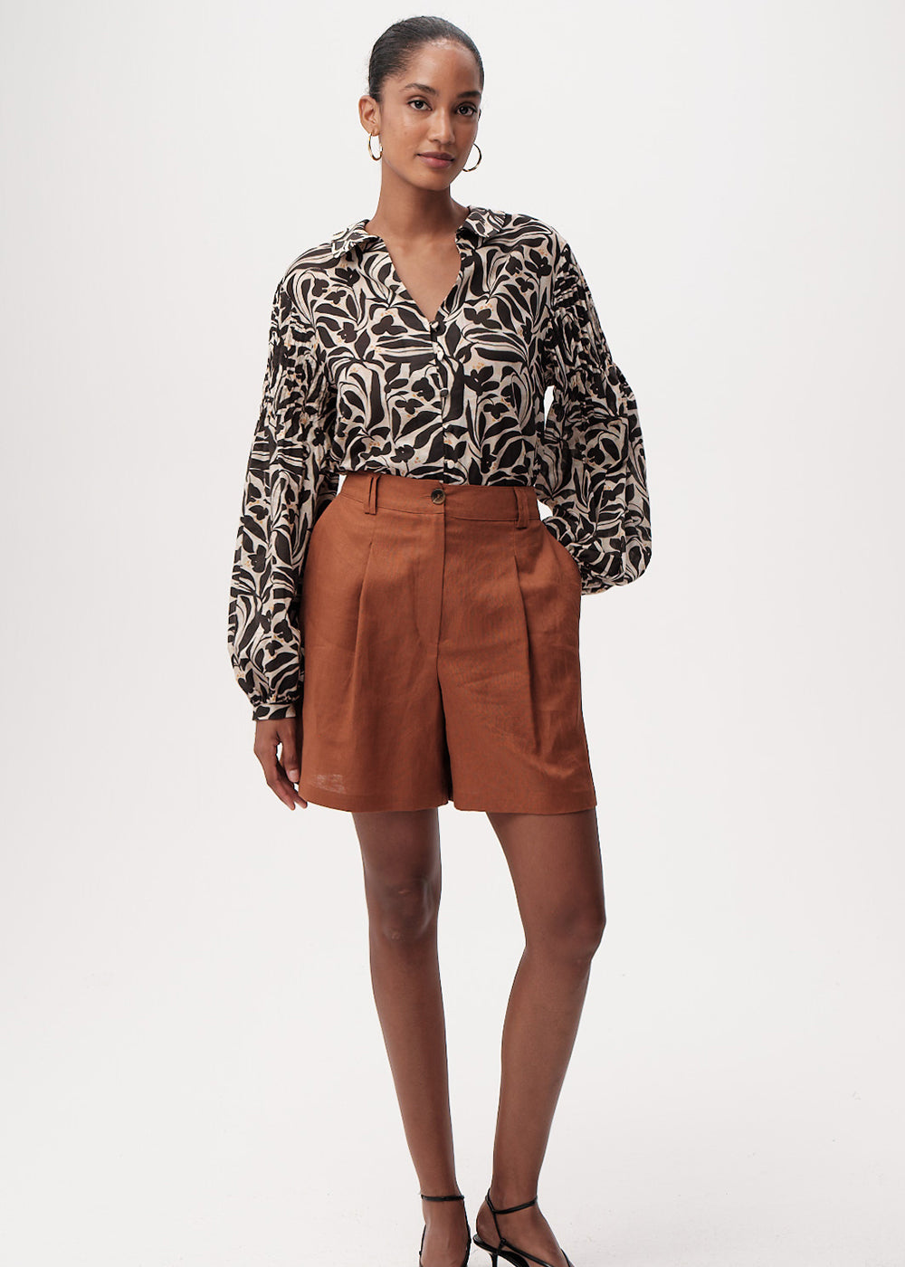 Woman wearing a patterned blouse and brown shorts on a white background