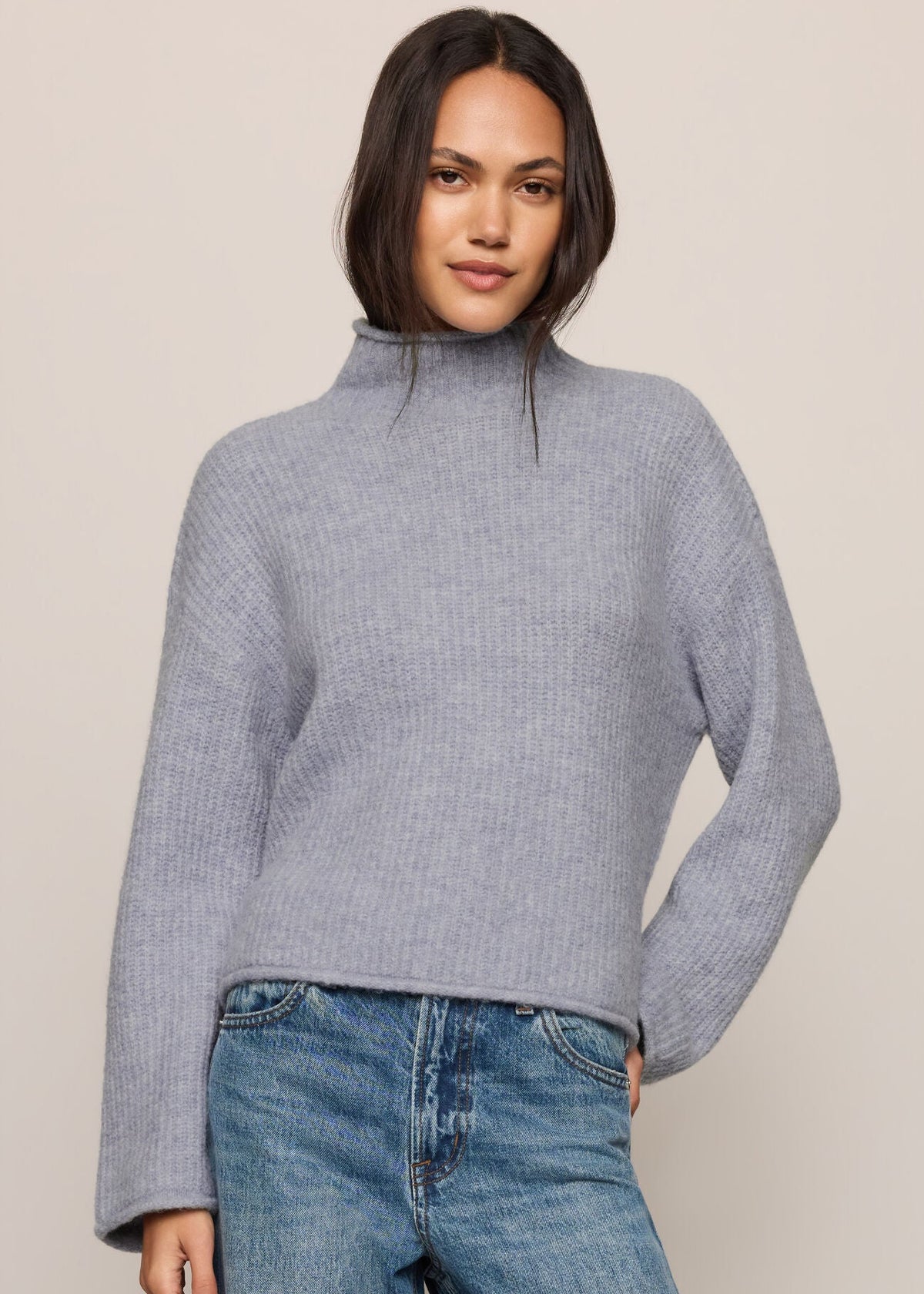 Woman wearing a gray sweater and blue jeans against a beige background
