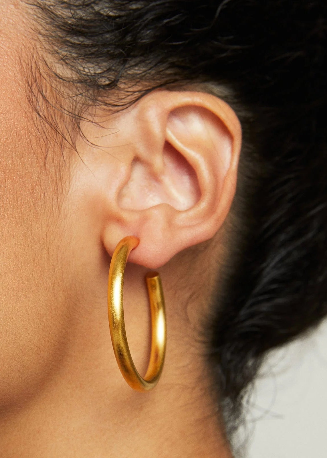 Gold hoop earring worn by a person with dark hair.