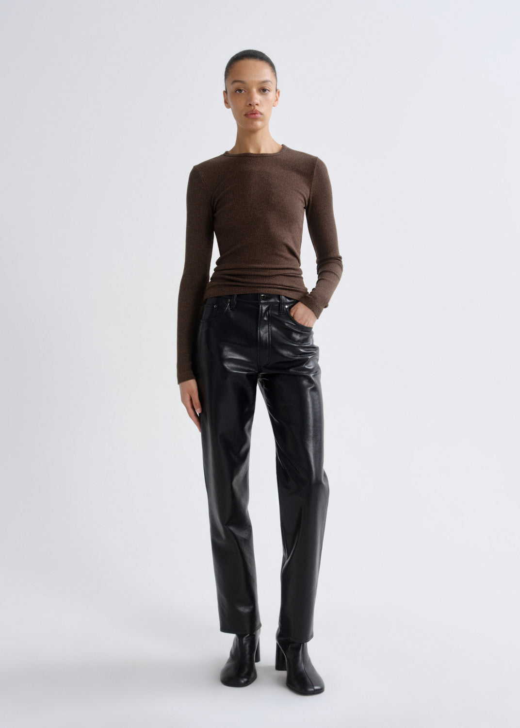 Person wearing a brown long-sleeve top and black leather pants on a white background