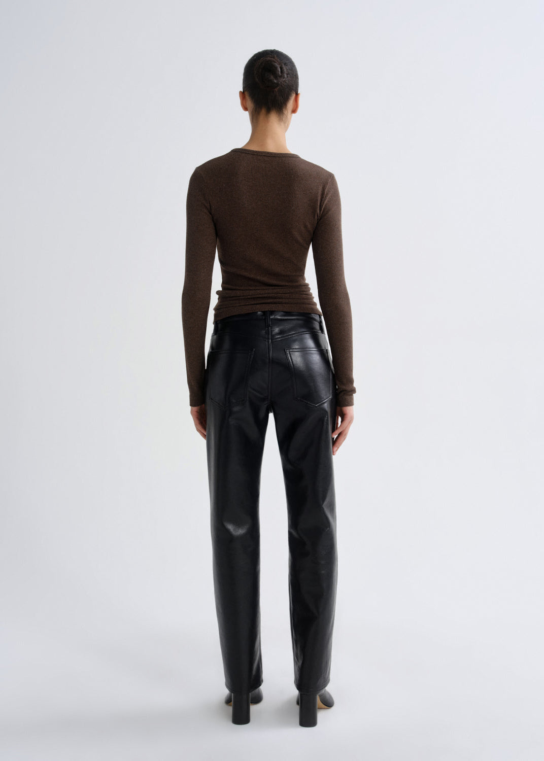 Person wearing a brown long-sleeve top and black leather pants on a white background
