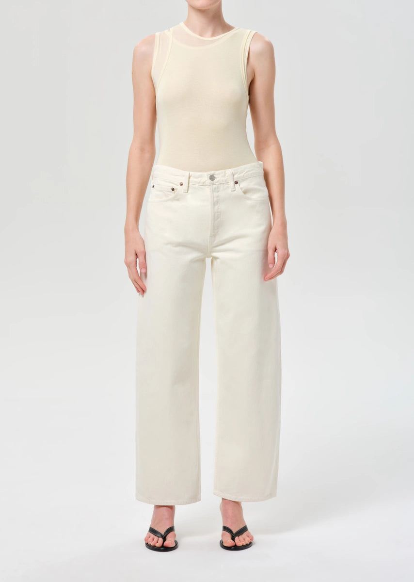 Person wearing a beige sleeveless top and white wide-leg jeans on a white background