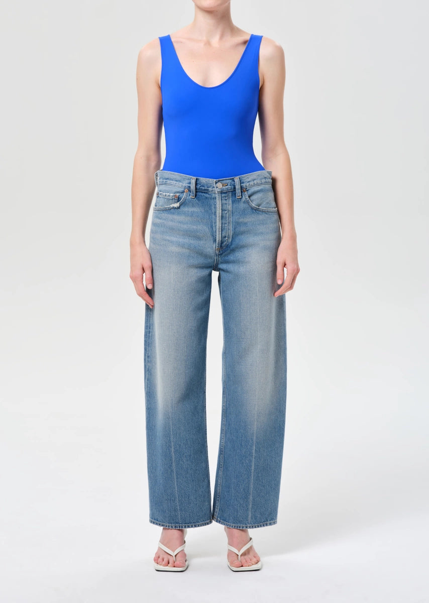 Person wearing a blue bodysuit and light blue jeans on a white background