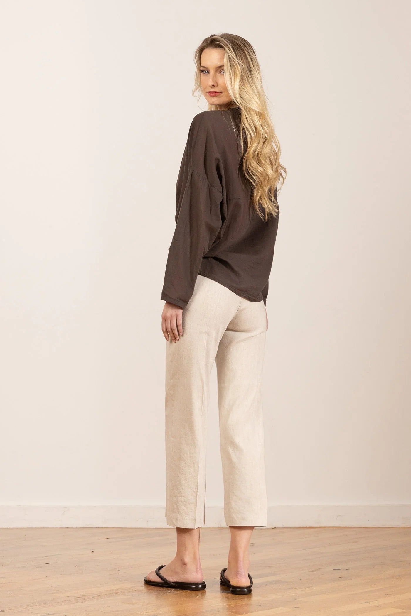 Woman wearing a brown sweater and beige pants against a plain background