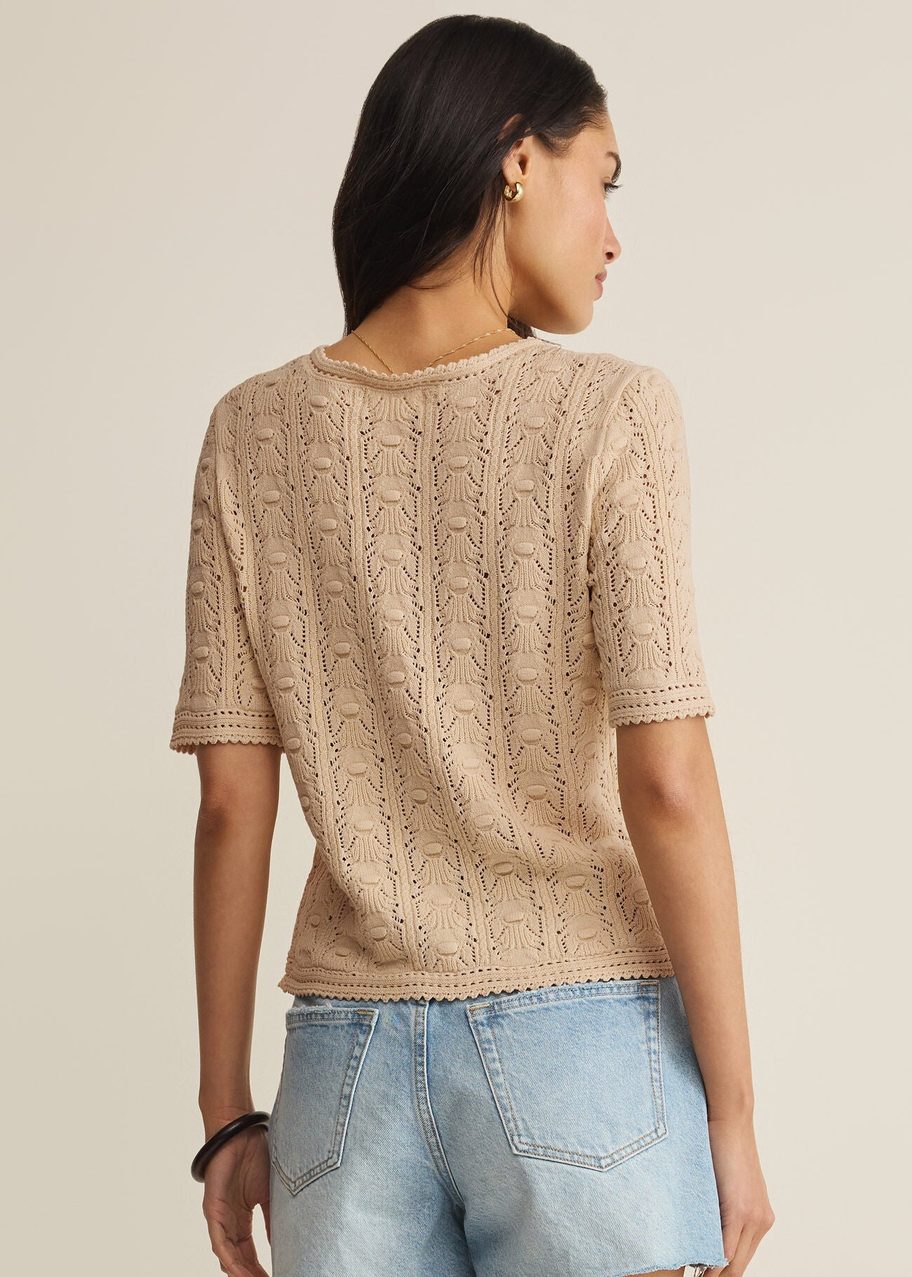 Woman wearing a beige knitted top and denim shorts on a plain background