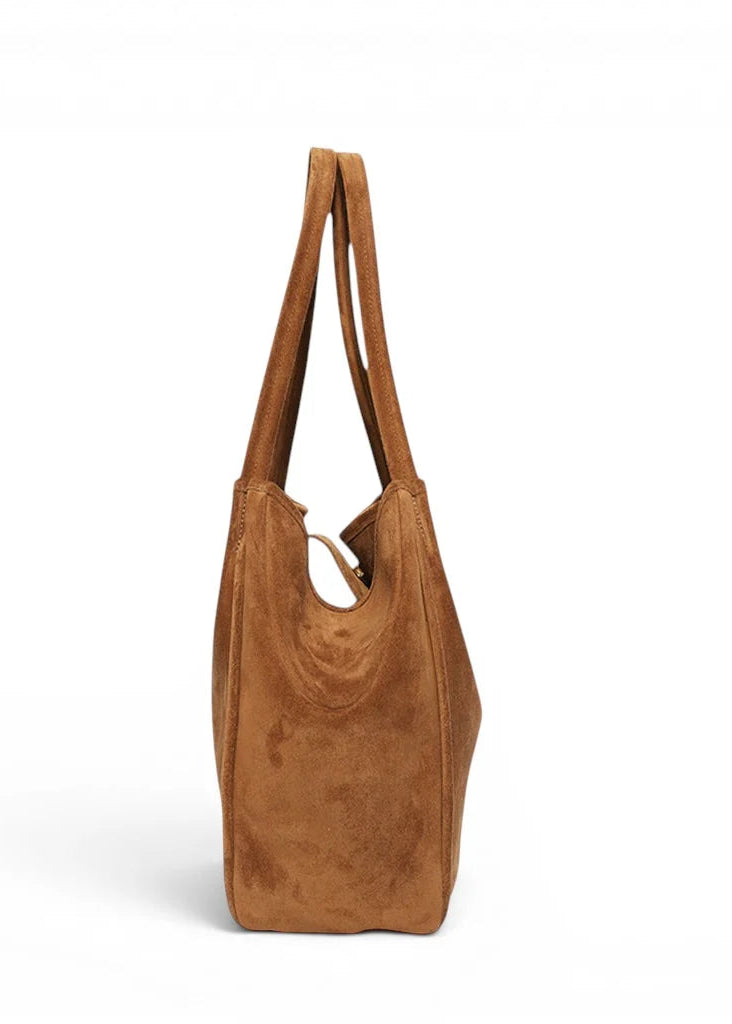 A tan suede slouchy tote bag with long shoulder straps, shown from a side profile against a clean white background.