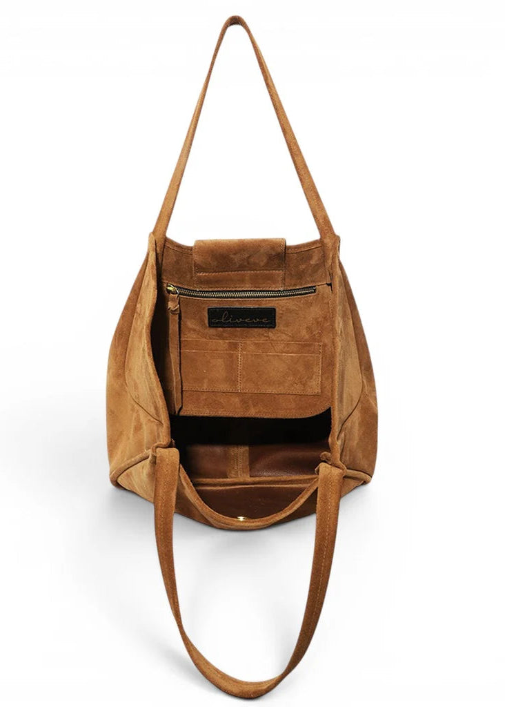 A tan suede shoulder bag shown from the front, with its front pocket open to reveal a black interior lining and a small black brand label that reads 'Sassano'.