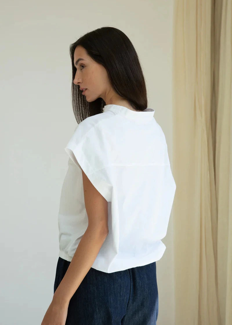 Woman wearing a white blouse and dark pants against a neutral background